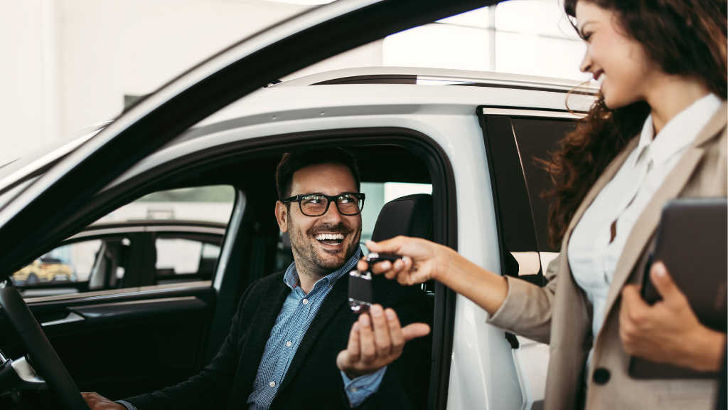 Autohändlerin gibt Mann im Auto Autoschlüssel und zeigt wie einfach es ist, ein Auto zu finanzieren.