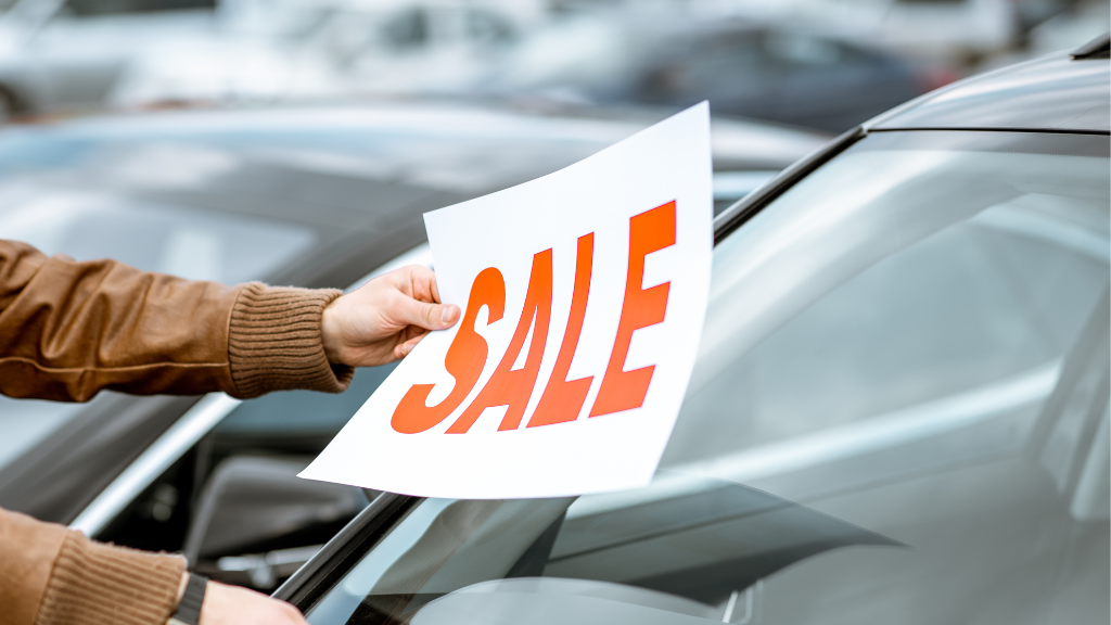 Ein Sale-Schild wird vom Verkäufer ans Auto angebracht