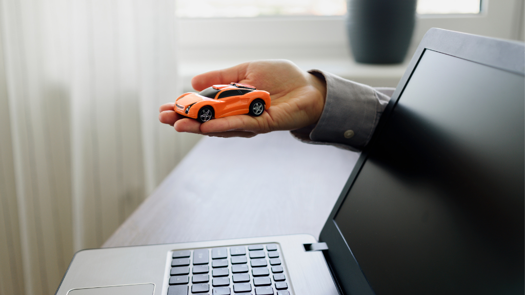 Hand mit Spielzeugauto kommt aus Laptop. Es symbolisiert den Online Vertragsabschluss für Autokredite